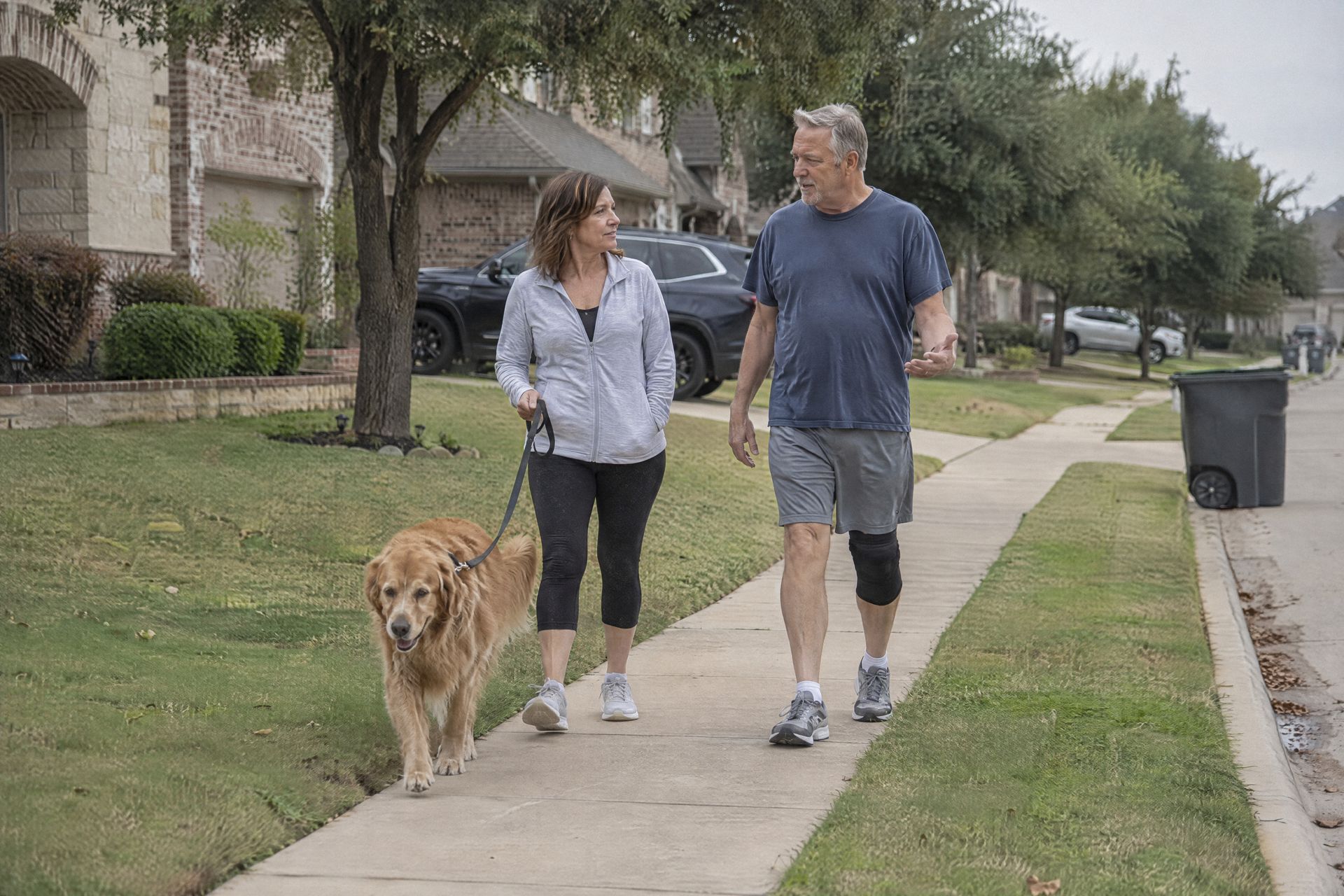 A couple walks their dog on a neighborhood sidewalk