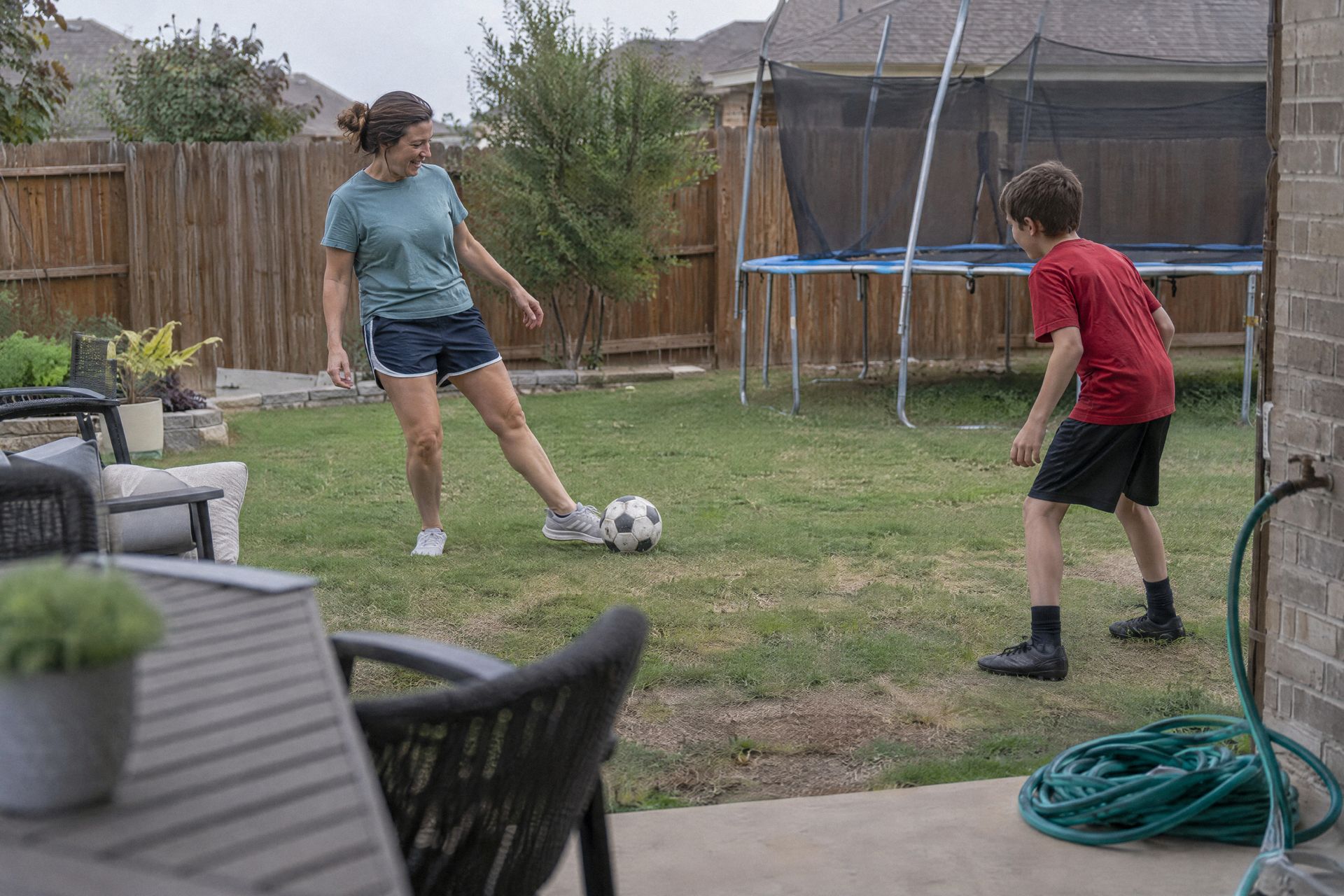A mom passes a soccer ball to her son in the backyard